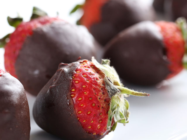 Fresh strawberries dipped in dark chocolate on blue wooden backg
