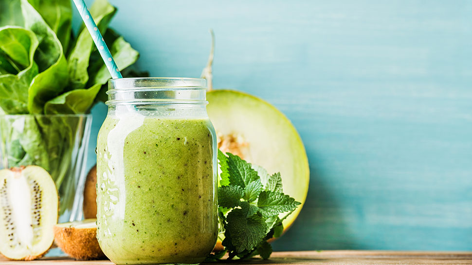 Freshly blended green fruit smoothie in glass jar with straw
