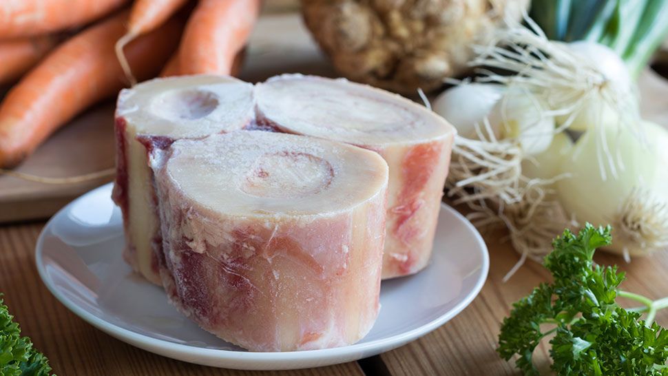 Beef marrow bones ready for broth, surrounded by fresh, mirepoix vegetables and herbs.