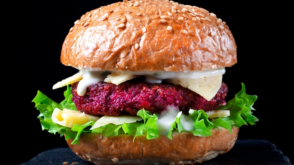 a beet burger with lettuce and cheese on a hamburger bun against a black background