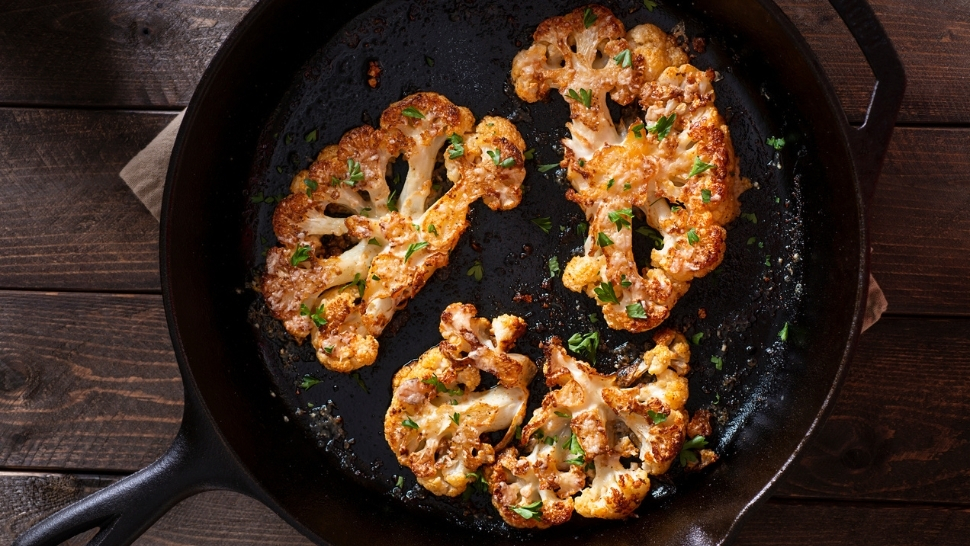 cauliflower steaks in a cast iron skillet on a wooden table