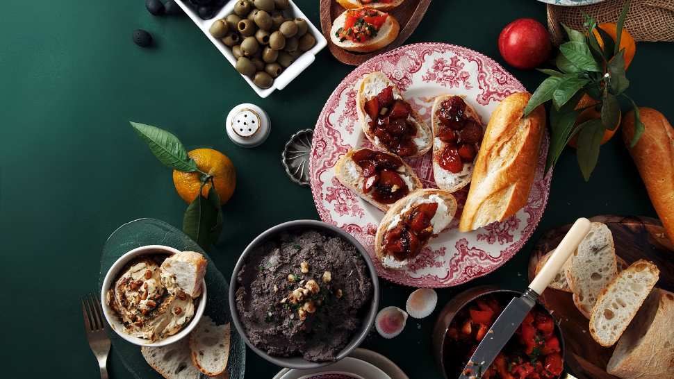 A cozy spread of rustic breads, savory dips, olives, and festive bruschetta, highlighting plant-forward holiday foods.