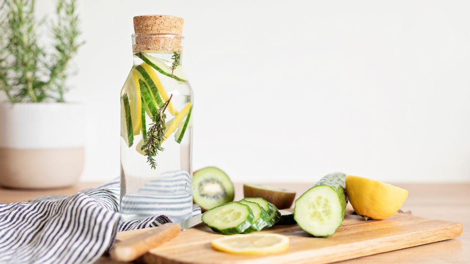 Corked bottle of cucumber lemon water with fresh herbs and striped napkin.