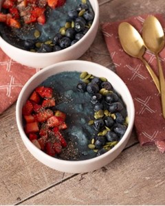 Homemade cornmeal bowls with fresh berries and juniper on a wooden table.