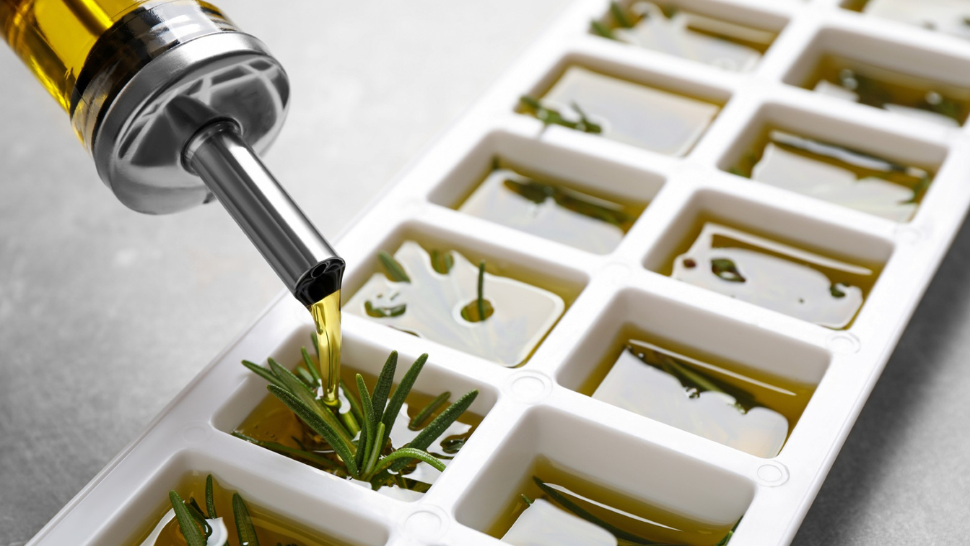 Olive oil poured into an ice cube tray with rosemary sprigs, preserving herbs in oil for sustainable cooking.