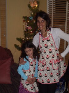 Owner of Outrageous Baking, Pamela Fletcher, alongside her daughter donning matching kitchen aprons.
