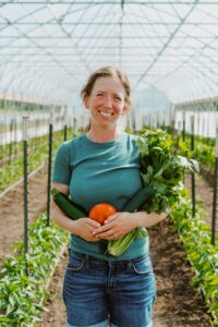 Seeds Farm founder Becca Carlson standing in a greenhouse holding freshly picked produce.