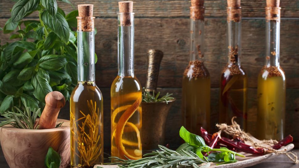 An assortment of herbs and food scraps, such as rosemary and a lemon peel, are infusing the bottles of oil with flavor.