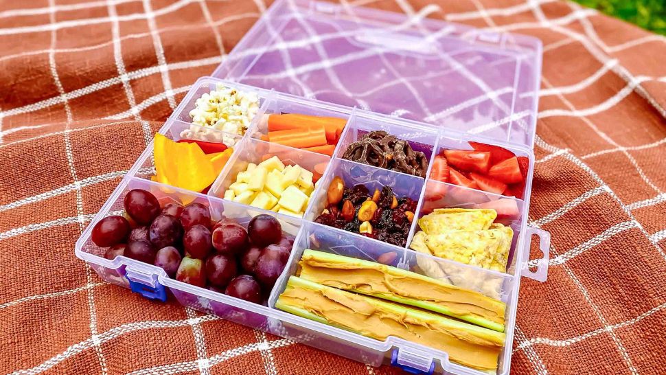 Colorful snackle box packed with fruit, crunchy veggies, cheese cubes, and trail mix.
