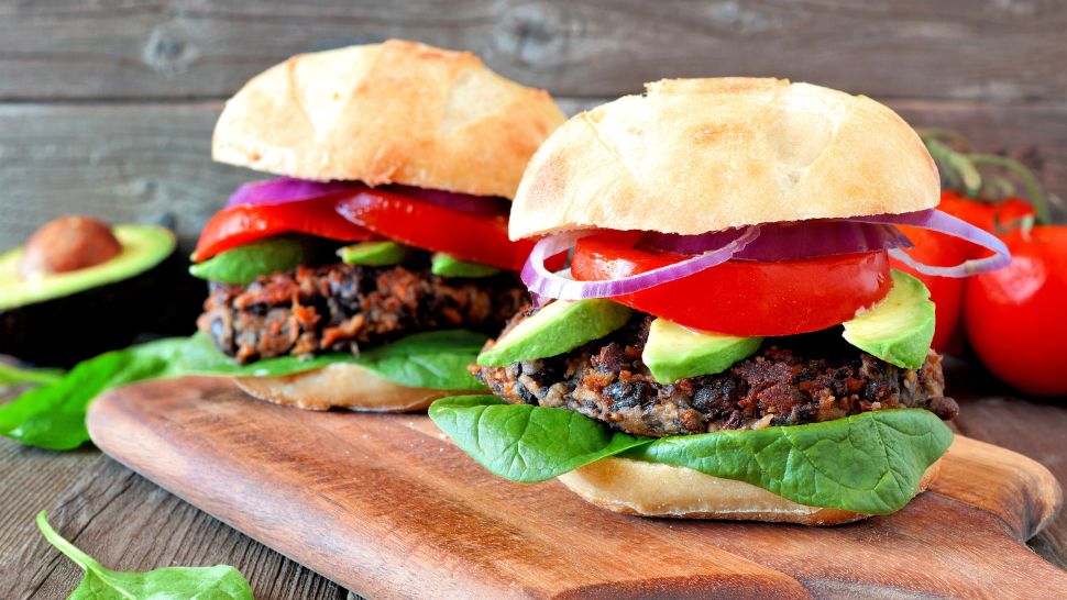 Grilled black bean burgers stacked with avocado, tomato, onion, and greens on rustic rolls.