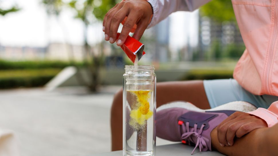 Person adding electrolyte powder to water bottle for post-exercise recovery.
