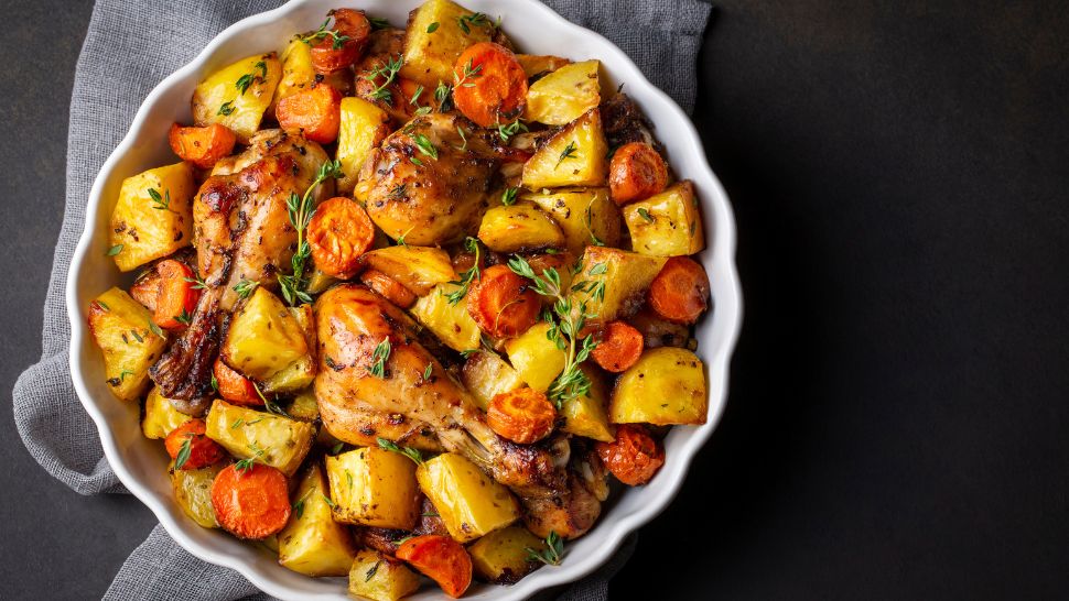 Golden roast chicken with potatoes and carrots, seasoned with fresh herbs.