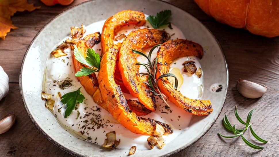 Charred squash on creamy yogurt with garlic and rosemary, set on a wooden table.