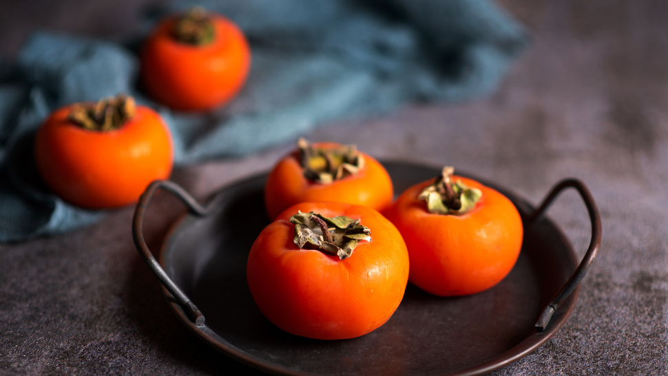 Ripe persimmons arranged on a metal tray with cozy fall lighting.