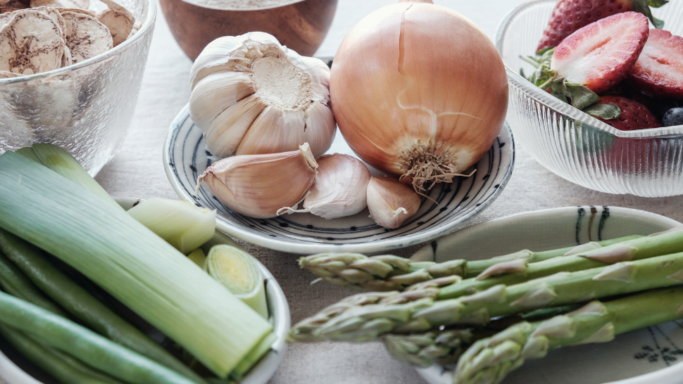 Fresh cooking ingredients including onion, garlic, leeks, asparagus, mushrooms, and strawberries arranged on a table