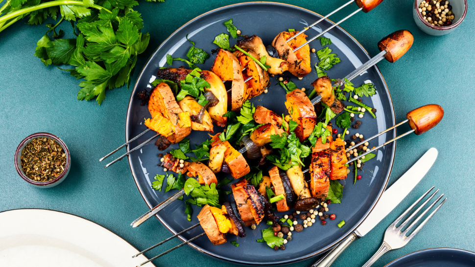 Grilled vegetable skewers with sweet potatoes, mushrooms, and onions, garnished with fresh parsley on a serving plate.
