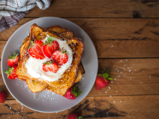 French toast with fresh strawberries, coconut shreds and honey, on wooden background, top view, text space, copy space
