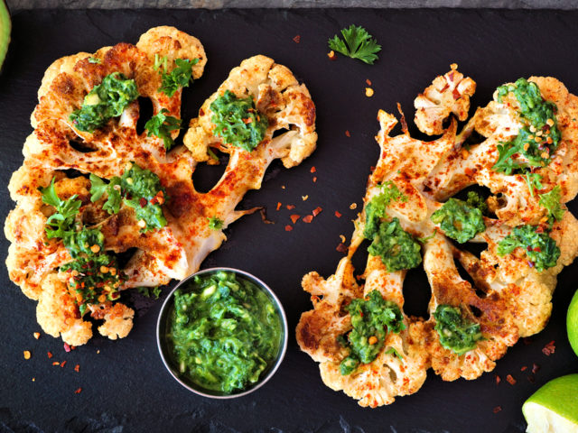 Cauliflower steaks above view on a slate platter, healthy plant based meat substitute concept